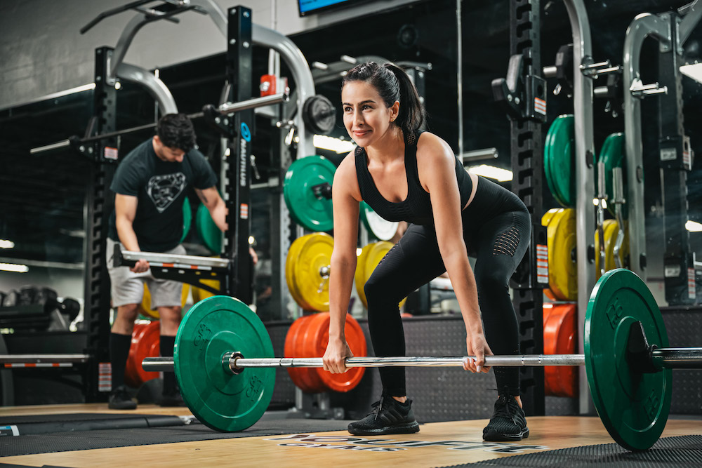 A smiling fit woman deadlifts a barbell